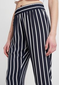 Tygbyxor i marinblått och vitt randigt mönster med resår i midjan och en texturerad kant. Tyget verkar lätt och flödande.