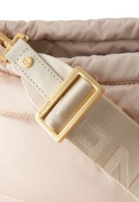 Borsa trapuntata rosa chiaro con tracolla regolabile color crema, fibbia dorata e dettaglio del logo sulla trama intrecciata della tracolla.