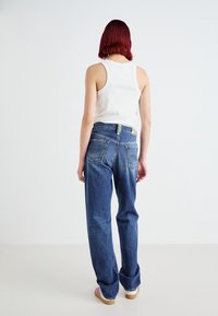 Lätt vit ribbad linne topp som kombineras med avslappnade blå denimjeans med bakfickor och en urtvättad look. Lätta träklackar.