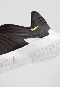 Czarne buty sportowe z fakturowanej tkaniny i białą gumową podeszwą. Wyposażone w jaskrawozielony akcent oraz wyraźne logo Nike na podeszwie.