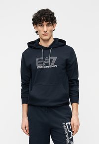 Marinblå huvtröja i bomullsblandning med framficka, dragband och vit broderad EA7 Emporio Armani-logotyp på bröstet.