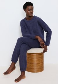 Navy quiltad loungewear-set som består av en avslappnad långärmad topp och byxor med elastiska mudd, tillverkad av mjukt, texturerat tyg.