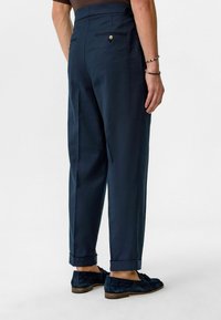 Navy broek met een iets ontspannen pasvorm, voorzien van opgerolde manchetten, twee achterzakken en een knoopdetail bij de taille. Zachte stofstructuur.