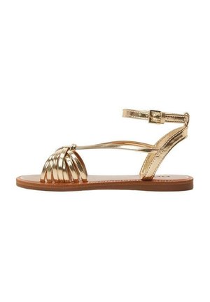 Guldmetallisk sandal med en flätad design vid tån, justerbart ankelsnöre och platt brun sula. Slät textur, minimal stil.