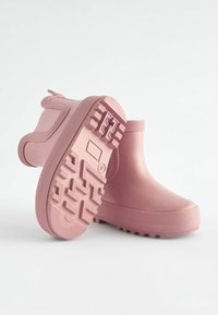 Bottes de cheville en caoutchouc rose avec une semelle texturée, un bout arrondi et des accents latéraux distincts. Fini lisse avec de légères paillettes tout au long.