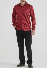Chemise en satin rouge à manches longues avec col pointu et boutonnière sur le devant, portée sur un pantalon noir et des chaussures noires. Texture lisse et brillante.