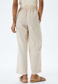 Pantalones beige a rayas con cintura elástica, diseño de pierna ancha y textura suave. Combinados con zapatos tipo slip-on de color claro.
