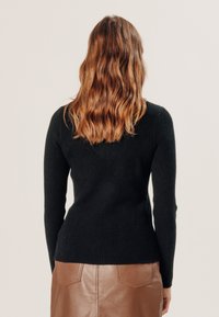 Zwarte geribbelde trui met lange mouwen, aangesloten bij de taille. Gecombineerd met een bruinen leren rok met zakdetails.