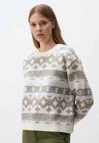 Fleece sweater in cream with geometric patterns in beige, blue, and gray. Features a round neck and ribbed cuffs and hem. Textured fabric.