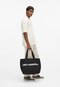Sac cabas noir avec deux anses robustes et logo blanc "KARL LAGERFELD" à l'avant. Fabriqué en tissu durable, avec un design spacieux.