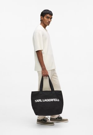 Melna tote soma ar divām izturīgām siksnām un baltu "KARL LAGERFELD" logotipu priekšpusē. Izgatavota no izturīga auduma, ar plašu dizainu.