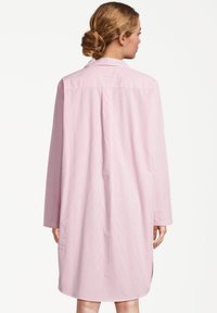 Abito chemisier rosa chiaro con maniche lunghe, colletto e fantasia a righe verticali. Presenta una vestibilità comoda e spacchi laterali per facilitare i movimenti.