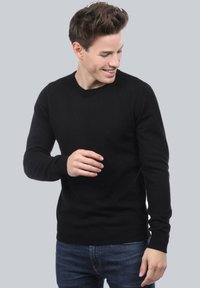 Pull noir à manches longues avec un col rond, fabriqué en tissu tricoté texturé, associé à un jean bleu. Design simple et ajusté.