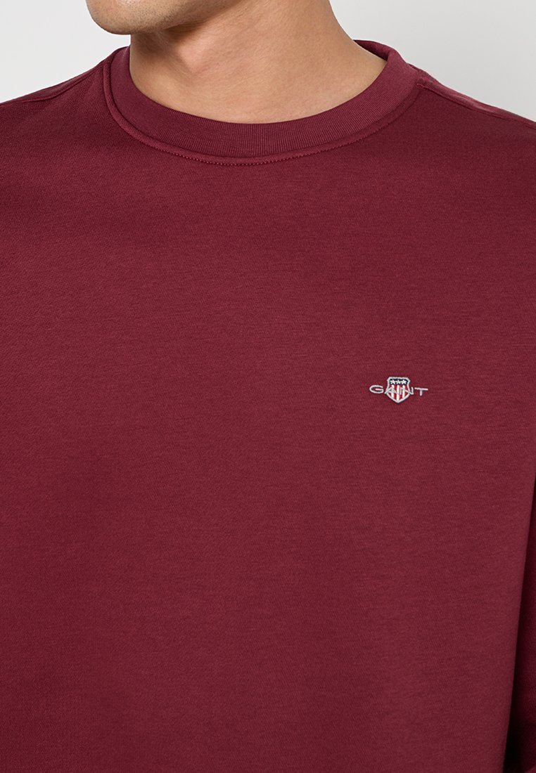 Sudadera burdeos de algodón suave, con un cuello redondo, puños acanalados y un pequeño logotipo bordado en el pecho.