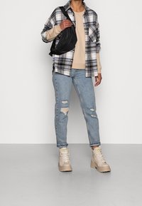 Rutig skjorta i marinblått och vitt, beige sweatshirt, slitna ljusblå jeans och beige högstövlar. Inkluderar en svart crossbody-väska.