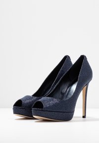 Décolleté in blu navy con tacco a platform, realizzati in tessuto testurizzato, caratterizzati da un design elegante e un tacco a spillo per aumentare l'altezza.