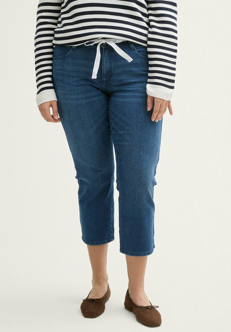 Dark blue cropped jeans with a smooth texture and slight stretch, paired with a black-and-white striped top featuring a tied waistband.