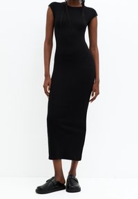 Černé maxi šaty bez rukávů s přiléhavým střihem, vyrobené z elastického materiálu. V kombinaci s černými skládacími botami s dekorativním kováním.