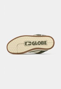 Semelle d'une basket avec une bande de roulement beige et marron, un motif antidérapant et le logo « GLOBE » au centre sur un fond blanc.