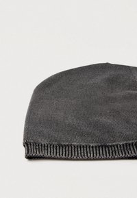 Adīta pelēka cepure ar gludu tekstūru un ribainu aproci. Apaļais augšējais gals ir ar viengabalainu dizainu bez redzamām šūšanas detaļām.