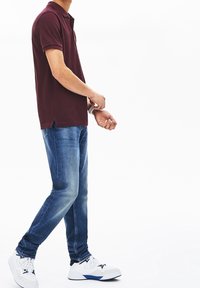 Polo bordeaux à manches courtes, associé à un jean en denim bleu et des baskets blanches avec des accents noirs et bleus.