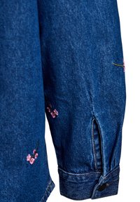 Chaqueta de mezclilla con bordado floral rosa en las mangas, cierre de botón estándar y detalle de abertura cerca de los puños.