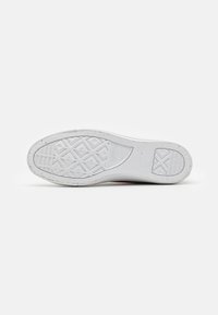 Sola de tênis branca em borracha com um padrão de grip texturizado e pequenas manchas. Apresenta um design de cravo em forma de diamante para tração.