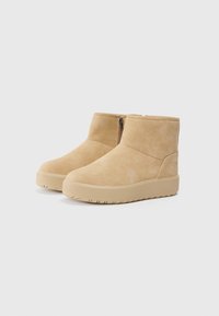 Bottines en suede beige avec une texture lisse, fermeture éclair latérale et semelle en caoutchouc épaisse à motif nervuré.