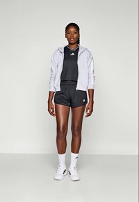 Grå zip-up hettegenser, svart treningstopp, svarte shorts, hvite sokker og hvite joggesko. Merkbar Adidas-profil på klærne og skoene.