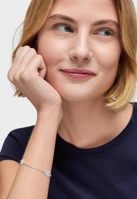 Bracciale d'argento con accentuazioni floreali su una delicata catena, indossato su un polso, abbinato a una maglietta blu navy.