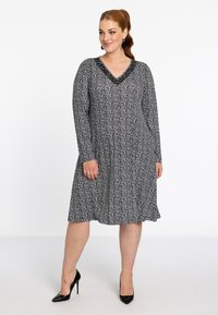 Robes à motifs noir et blanc avec des manches longues, décolleté en V et encolure texturée. Forme évasée en A, associée à des escarpins noirs.