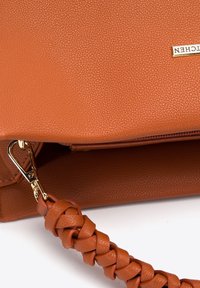 Brown textured leather handbag with braided strap and gold metal clasp, partially open on white background.