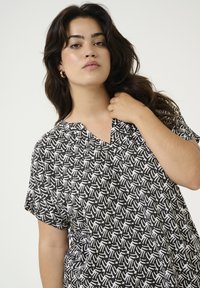 Haut noir et blanc à motifs avec un décolleté en V, des manches courtes et une coupe décontractée. Le tissu présente un motif manuel répété.