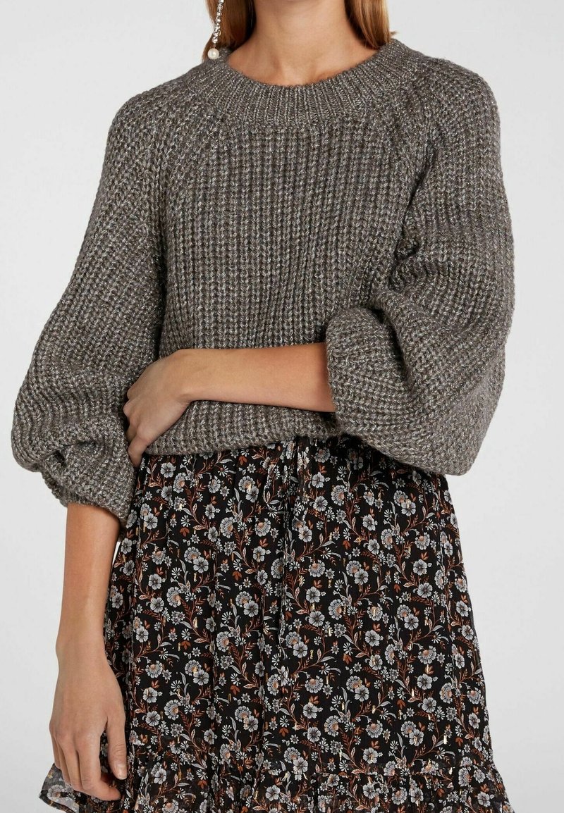 Szary sweter z prążkowanego dzianiny z bufkami na rękawach, noszony na czarnej spódnicy w kwiatowy wzór z małymi kwiatami i falbaną na dole.