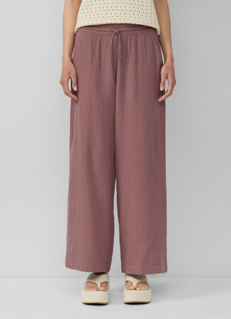 Pantalons larges à coupe décontractée en mauve, en tissu texturé, avec une taille élastique et un cordon de serrage. Associés à des sandales compensées.