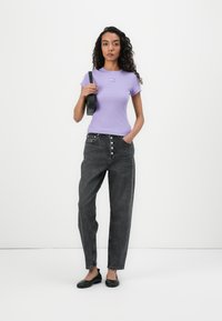 T-shirt violet à manches courtes en côte avec un petit motif, associé à un jean en denim gris foncé à taille haute, avec une fermeture par boutons et des jambes larges.