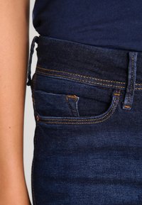 Sötétkék, slim fit denim farmernadrág, elöl egy kis zsebbel, narancssárga varrással és klasszikus öt zsebes dizájnnal.