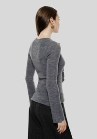 Maglione grigio lavorato a maglia con maniche lunghe e design aderente, caratterizzato da un dettaglio testurizzato sulla parte anteriore. Indossato con pantaloni scuri.