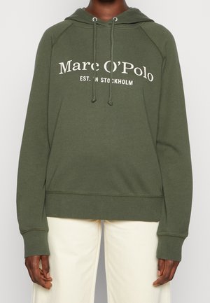 Personne portant un sweat à capuche Marc O'Polo vert olive avec cordons et un pantalon beige, visible du cou aux hanches sur fond uni.