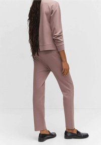 Sudadera rosa recortada y pantalones ajustados a juego. Tela suave con textura mínima. El modelo lleva mocasines negros, mostrando una silueta estilizada.