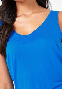 Mouwloze top met V-hals in felblauwe stof. Soepele textuur, aansluitend ontwerp, met een schone snit rond de halslijn en schouders.