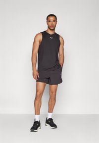 Czarny sportowy tank top z małym białym logo, w połączeniu z ciemnymi szortami i czarnymi butami. Skupienie na wydajności sportowej i cechach komfortowych.