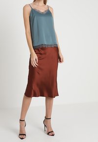 En turkos satinlinne med spetsdetaljer matchas med en rostfärgad satinkjol, som har en mjuk textur och en smal silhuett, bärs med svarta klackar.