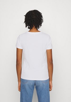 Camiseta de algodón blanca con mangas cortas, cuello redondo y silueta ajustada, combinada con jeans de mezclilla azul claro.