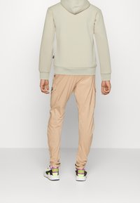 Felpa leggera beige con cappuccio regolabile, abbinata a pantaloni cargo pesca chiaro con tasche laterali, indossata con sneakers multicolori.