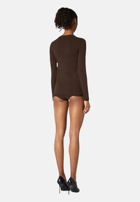 Brun långärmad topp i mjukt tyg, figursydd design, rund halsringning, tillsammans med svarta högklackade skor, visad från baksidan.