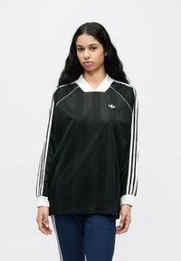 Čierny športový dres s dlhými rukávmi a bielymi detailmi, s výstrihom do V, vertikálnymi pruhmi a logom Adidas na hrudi.