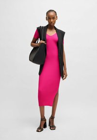 Dopasowana różowa sukienka z prążkowanym wzorem, z bocznym rozcięciem, nałożona pod czarną bezrękawnikową marynarką, uzupełniona czarną torebką i sandałami na obcasie.