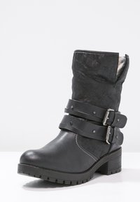 Černé kotníkové boty vyrobené z hladké syntetické kůže s mírně mačkaným povrchem, s dvěma nastavitelnými popruhy na přezky a nízkým podpatkem.