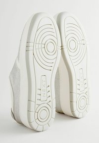 Weiße Sneaker mit strukturiertem, funkelndem silbernen Obermaterial und Gummisohlen, die kreisförmige Muster und ein Markenlabel an der Seite aufweisen.
